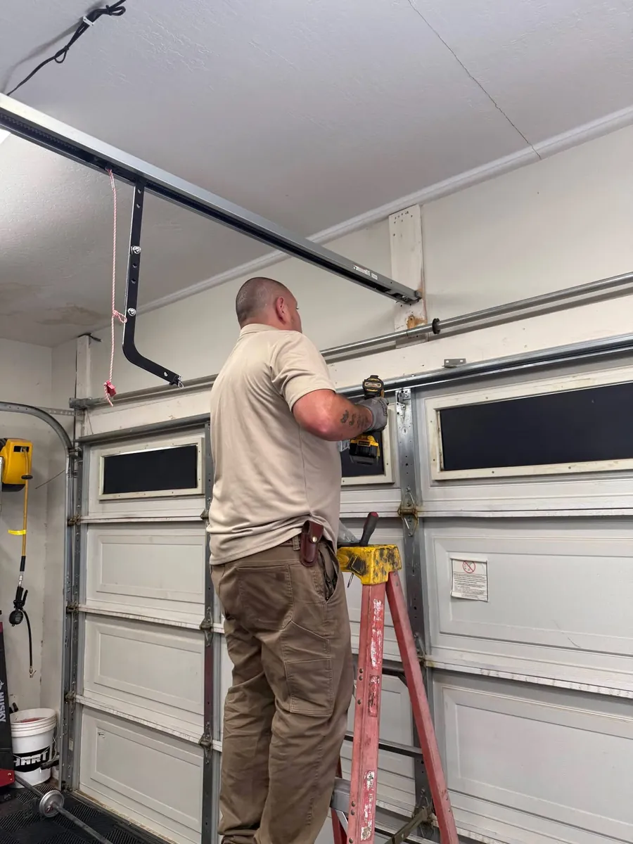 A technician working on the upper hardware of a residential garage door