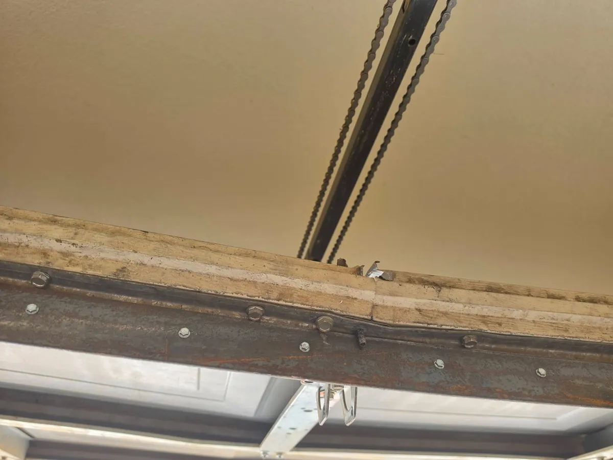 Close-up of a garage door top panel with worn reinforcement and mounting hardware